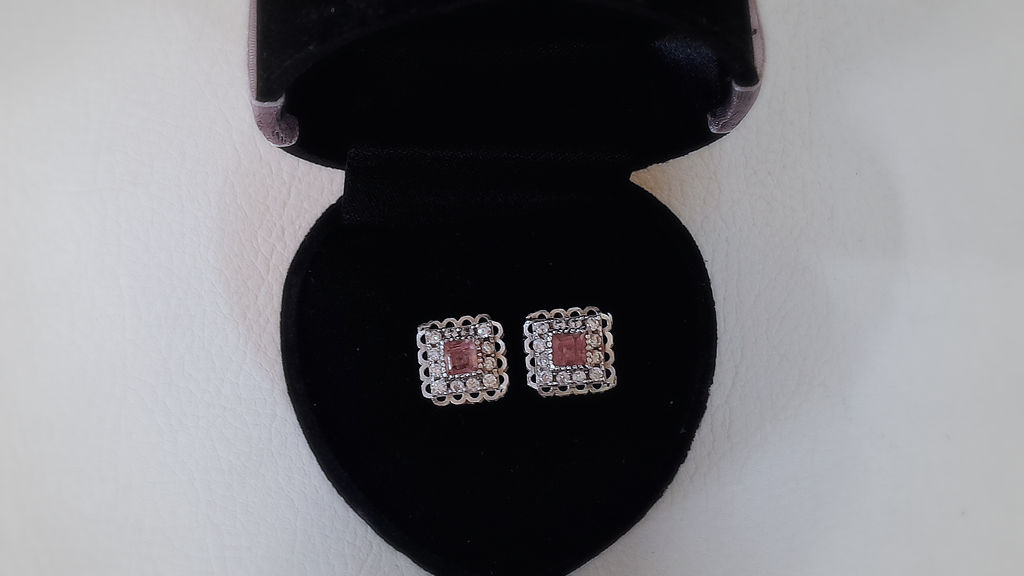 Pair of square earrings with red stones in a black jewelry box on a white background
