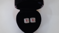 Pair of square earrings with red stones in a black jewelry box on a white background