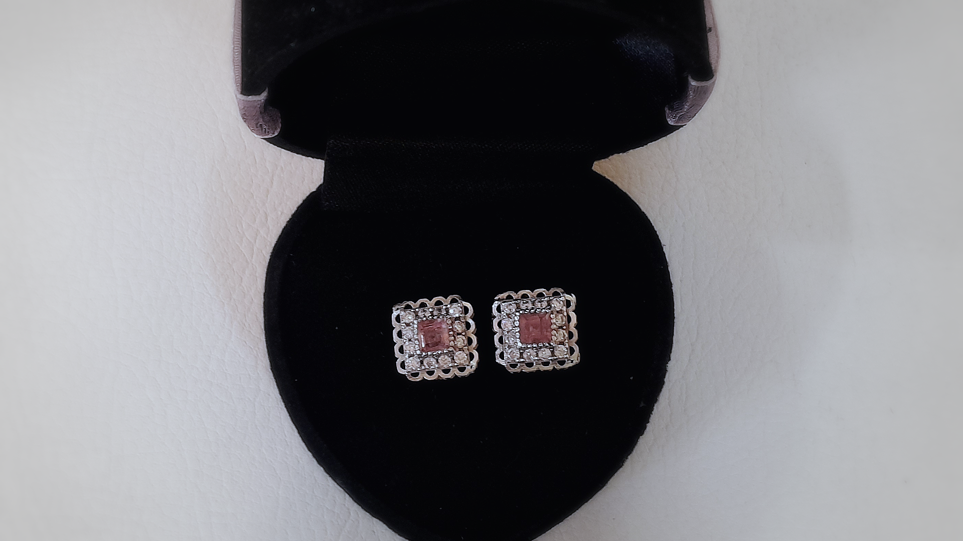 Pair of square earrings with red stones in a black jewelry box on a white background