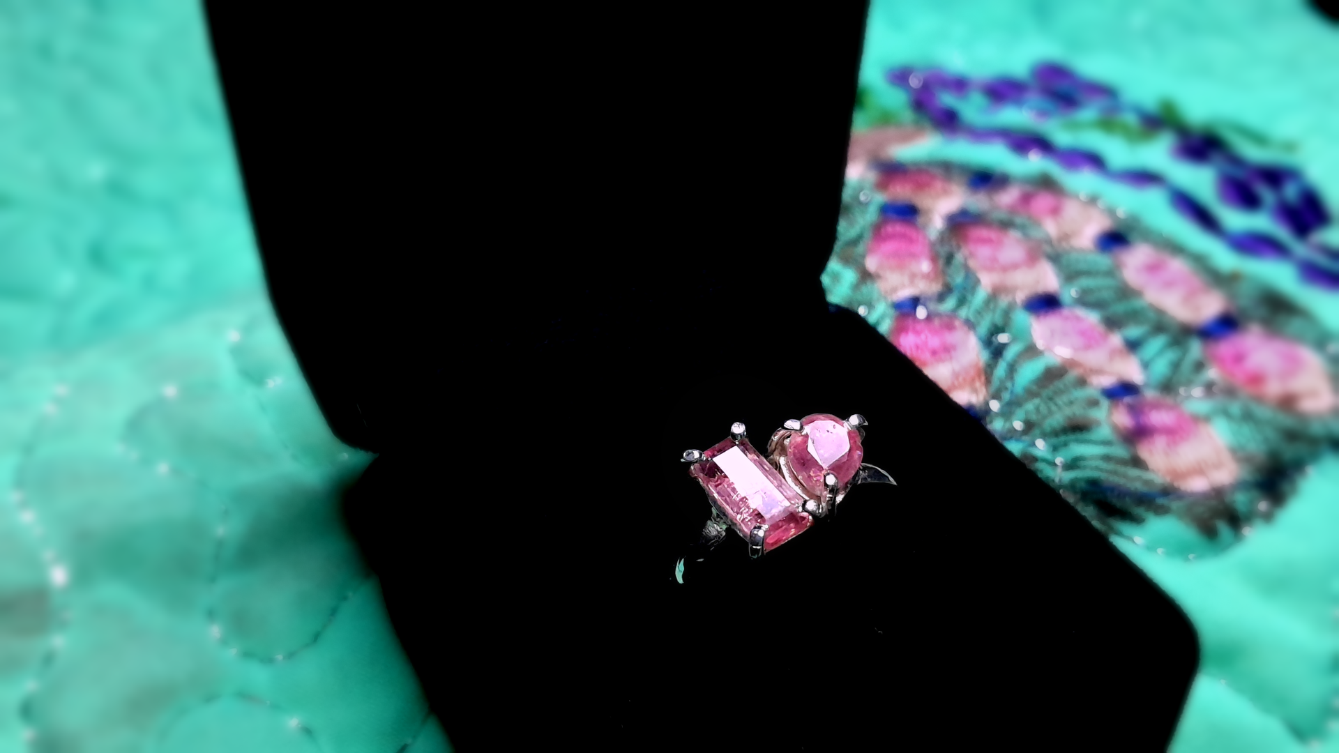 Pink tourmaline gemstone ring in an open black box on a teal fabric background